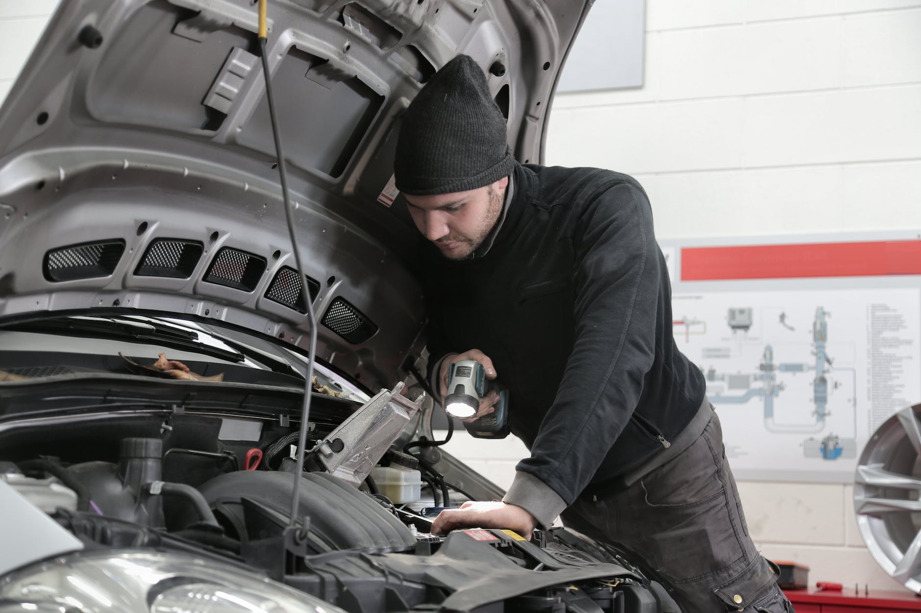 man in black jacket and black knit cap inspecting car engine